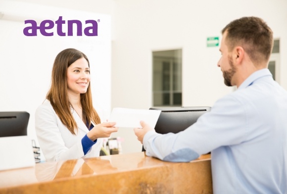 Dental team member taking patients insurance card with Aetna logo in background
