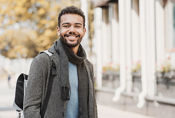 Man in jacket and scarf walking outside while smiling