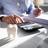 Man using calculator and writing on paper; tooth next to calculator