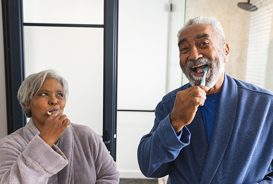 a smiling couple in bath robes brushing their teeth together