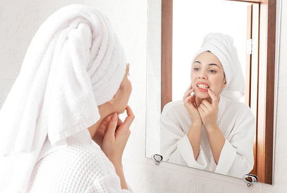 Woman in white robe looking at gums in reflection