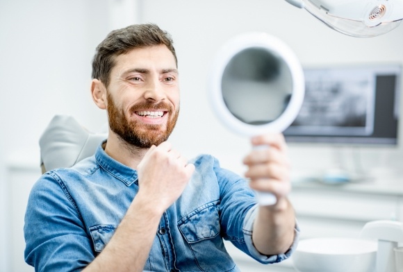 Man looking at healthy smile in mirror after gum disease treatment