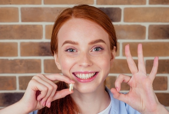 Smiling young woman holding up wisdom tooth extractions