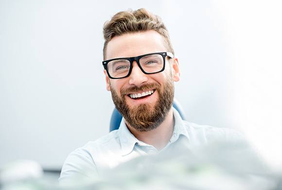 Bearded man with glasses sitting in dental chair and smiling