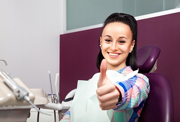Yong woman giving a thumbs up in dental chair