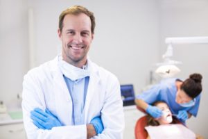 a dentist smiling while a patient has their teeth checked by a dental hygienist 