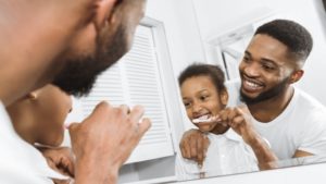 parent helping their child brush their teeth in a bathroom mirror
