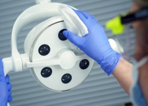 a dental team member disinfecting an overhead light before a new patient arrives