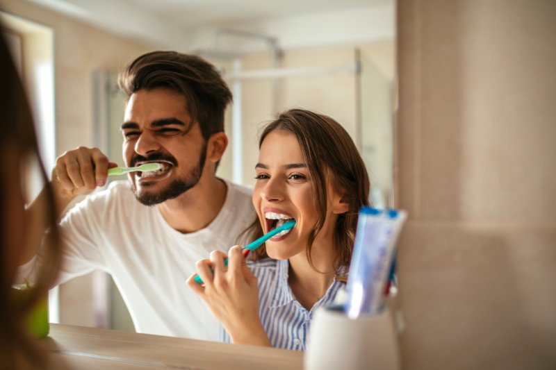 Couple smiling while brushing their teeth