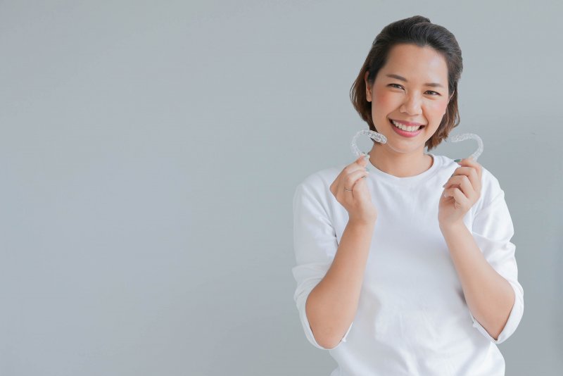 woman smiling and holding Invisalign in Carrollton