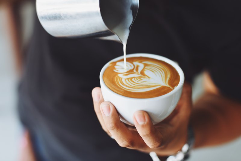 A barista making latte art in the shape of a heart